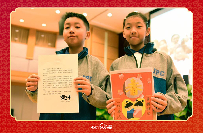 圖為香港“少年警訊”成員郭宏晞（左）展示習(xí)主席回信、羅顥凝（右）展示送給習(xí)主席的賀卡并合影。